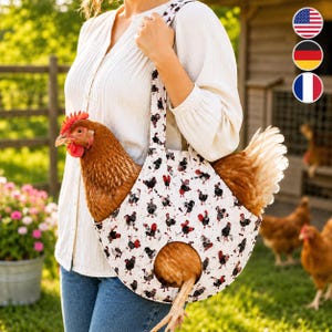 May include: A white fabric chicken carrier bag featuring a repeating pattern of small black and red roosters. The bag has a circular opening at the bottom for the chicken's legs and a shoulder strap, with a brown chicken resting inside the carrier.