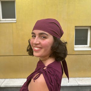 May include: A dark maroon and black gingham headscarf tied at the back of the head, paired with a matching sleeveless top featuring gathered fabric at the shoulders and thin tie closures. The fabric has a small-scale checkered pattern throughout.