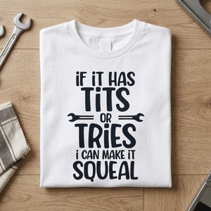 May include: A white short-sleeved t-shirt featuring black text that reads: IF IT HAS TITS OR TRIES I CAN MAKE IT SQUEAL, with two small wrench icons separating the words TITS and OR, and TRIES and I CAN MAKE IT SQUEAL.