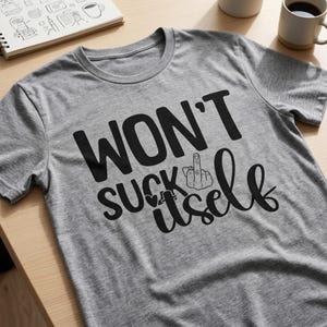 May include: A heather gray short-sleeved t-shirt featuring black text that reads WON'T SUCK itself, with a graphic of a hand making a middle finger gesture replacing the letter I and a small heart icon integrated into the design.