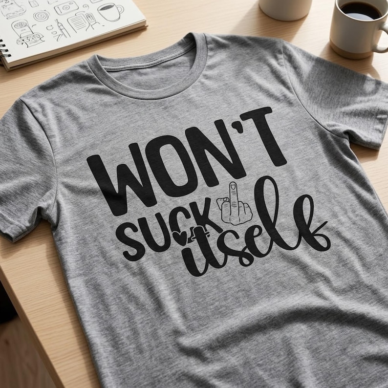 May include: A heather gray short-sleeved t-shirt featuring black text that reads WON'T SUCK itself, with a graphic of a hand making a middle finger gesture replacing the letter I and a small heart icon integrated into the design.