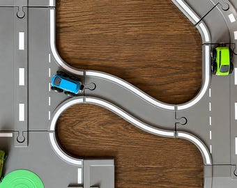 May include: A gray toy road track system with interlocking puzzle-style pieces featuring white lane markings. Three small toy cars in blue, lime green, and a green van with yellow accents are positioned on the curved and straight road sections.