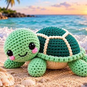 Op de afbeelding: Een gehaakt schildpad knuffeltje met een lichtgroene kop, een donkergroen schild met crèmekleurige stiksels en grote zwarte ogen. De schildpad heeft roze blosjes op de wangen en een geborduurde glimlach, geplaatst op een zandstrand met schelpen.