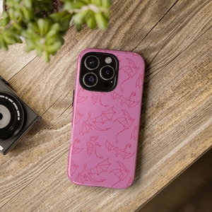 Puede incluir: Una funda de smartphone rosa con un patrón repetitivo de dragones dibujados con líneas de color rosa oscuro en varias poses de vuelo. La funda tiene un recorte negro para el módulo de cámara en la esquina superior izquierda, con tres lentes.