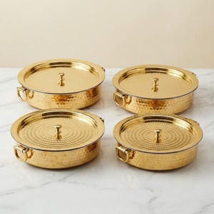 Puede incluir: Un juego de cuatro recipientes redondos de metal dorado con tapa. Cada recipiente presenta una textura martillada en el exterior, un pomo central en la tapa y dos pequeñas asas laterales. La superficie de cada tapa tiene un patrón circular.