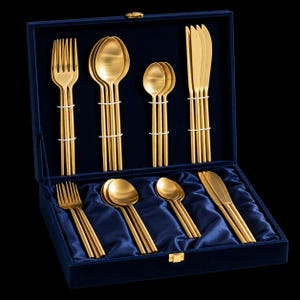 Könnte beinhalten: Ein goldfarbenes Besteckset aus Edelstahl, angeordnet in einer mit marineblauem Samt ausgekleideten Präsentationsbox. Das Set enthält Gabeln, Esslöffel, Teelöffel und Messer mit einer glatten, matten Oberfläche und schlanken Griffen.