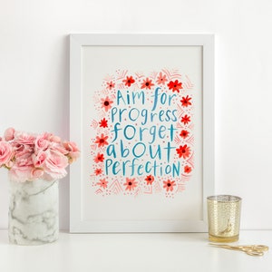 Könnte beinhalten: Weißer gerahmter Druck mit einem blauen und roten Aquarelldesign. Der Druck zeigt den Text "Aim for progress forget about perfection" umgeben von roten und rosa Blumen.