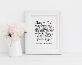 Puede incluir: Una impresión enmarcada en blanco con una cita inspiradora en blanco y negro que dice "Cling to Joy: Audacious and Unbridled Joy, That Looks for Light in everything. Even in your Waiting -Morgan Harper Nichole". Una jarra blanca con peonías rosas está en primer plano.