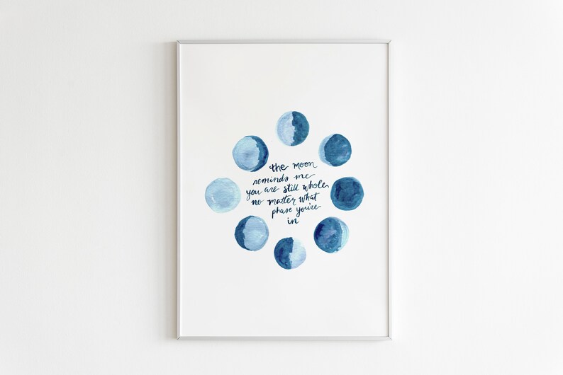 Op de afbeelding: Een aquarelprint met een cirkel van blauwe manen met de tekst "the moon reminds me you are still whole no matter what phase you're in".