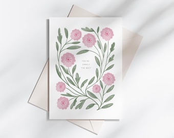 May include: Greeting card with a floral design featuring pink flowers and green leaves. The card reads "You're Simply The Best." The card is placed on top of a light pink envelope.