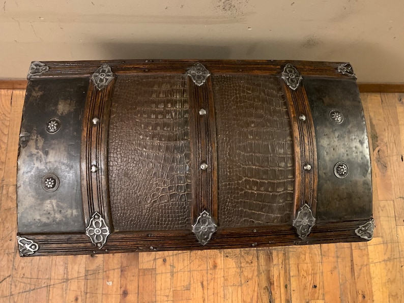 Pode incluir: Um ba&uacute; de madeira vintage com uma tampa de couro marrom com relevo de crocodilo. O ba&uacute; tem detalhes em metal e tachas decorativas de metal.