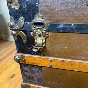 Three-quarter view of the antique travel chest, emphasizing its large size and rustic heritage aesthetic and original hardware