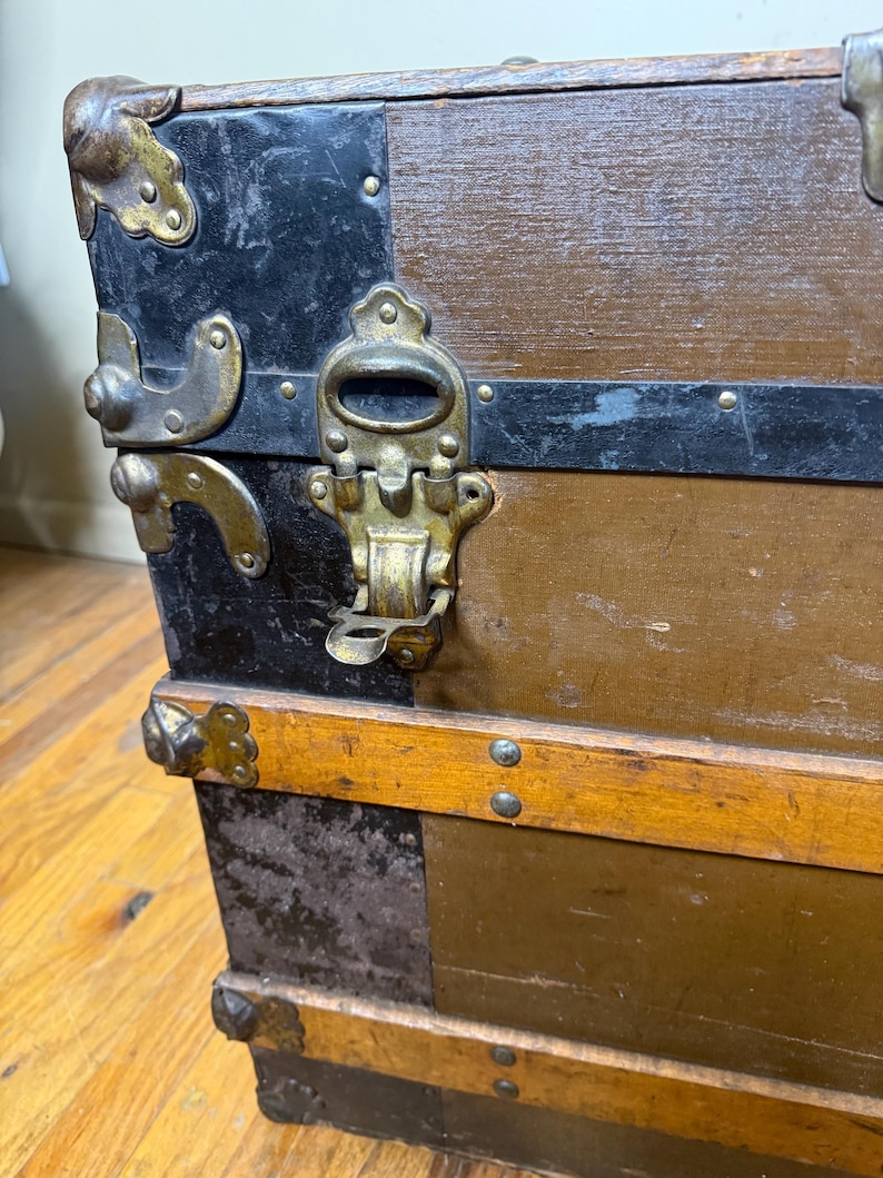 Three-quarter view of the antique travel chest, emphasizing its large size and rustic heritage aesthetic and original hardware