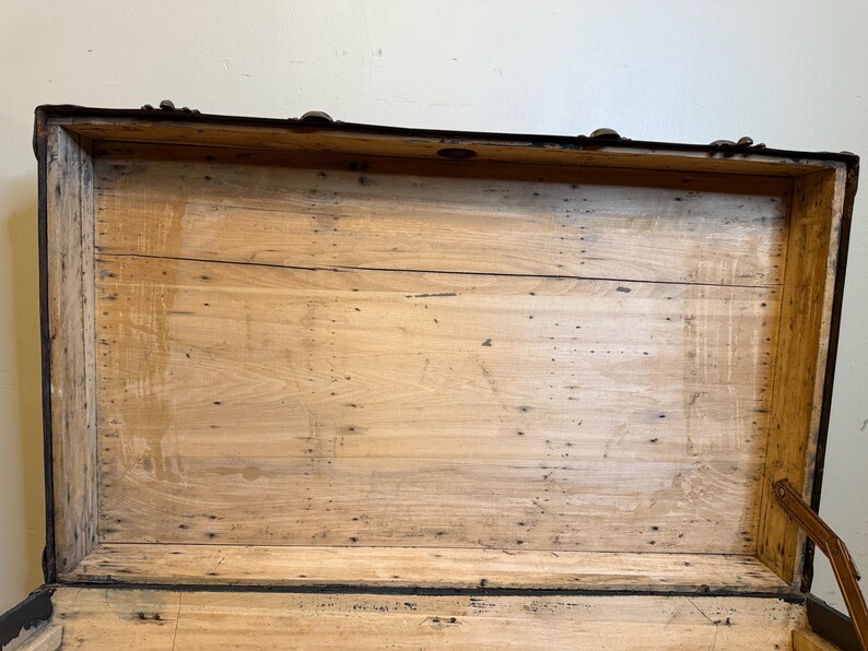 Puede incluir: Ba&uacute;l de madera antiguo abierto con interior marr&oacute;n claro. El ba&uacute;l tiene molduras y herrajes de metal oscuro. El interior est&aacute; hecho de tablas de madera de color claro. El ba&uacute;l est&aacute; abierto, revelando el interior.