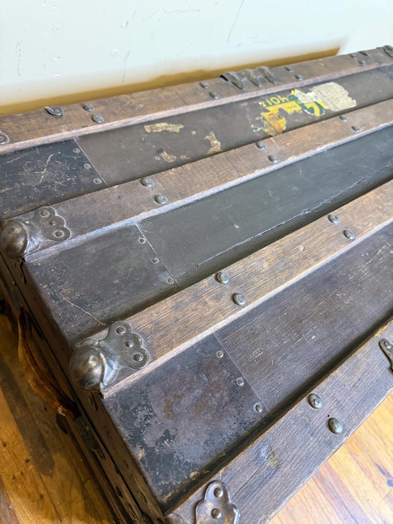 May include: Antique wooden trunk with metal accents. The trunk features dark wood slats, metal corner protectors, and a distressed finish. The metal is dark gray, and the wood is a medium brown. The trunk has a vintage aesthetic.