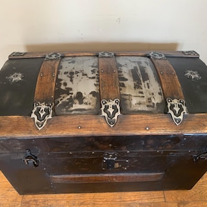 May include: Antique wooden trunk with metal accents and a distressed finish. The trunk has a curved lid and is secured with metal clasps.