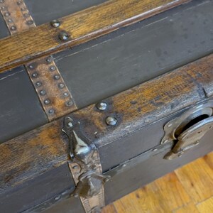 Puede incluir: Ba&uacute;l antiguo con paneles gris oscuro y molduras de madera. El ba&uacute;l presenta detalles met&aacute;licos, incluyendo protectores de esquina y remaches. La moldura de madera tiene un aspecto c&aacute;lido y envejecido.