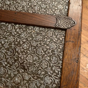 May include: Close-up of a wooden antique trunk with a silver floral patterned metal panel. The trunk has a decorative metal clasp.
