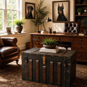 May include: A well-lit home office featuring a leather armchair, a wooden desk, and a vintage trunk. Two framed dog portraits hang on the wall. A small potted plant sits on the trunk, and a rug covers the floor.