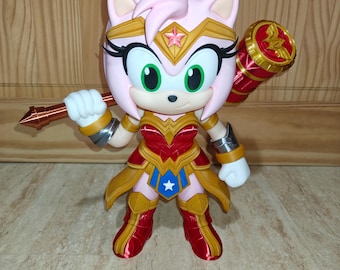 May include: A light pink hedgehog figurine dressed in a metallic red and gold superhero costume with a blue waist accent featuring a white star. The character wears a gold tiara with a pink star and holds a large red and gold hammer over one shoulder.