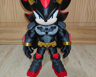 May include: A figurine of a black and red hedgehog character wearing a dark gray and black armored suit with a bat-shaped emblem on the chest, a gold utility belt, and red accents on the boots, gloves, and head, standing in a forward-facing pose.