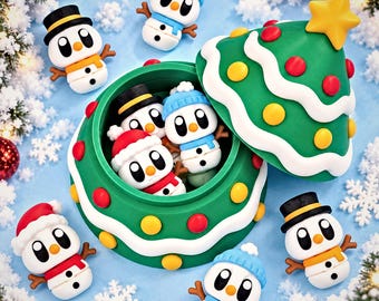 May include: A green Christmas tree-shaped container with a removable lid, decorated with yellow and red circular ornaments. Inside and surrounding the container are several small snowman figurines wearing hats and scarves in various colors.