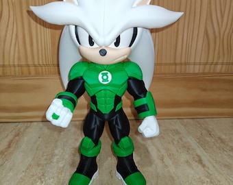 May include: A figurine of a character with white spiky hair wearing a green and black suit with a Green Lantern emblem on the chest. The character has white gloves, a green ring on the right hand, and black boots with green accents on the toes.