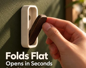 May include: A wall-mounted hook featuring a white rectangular frame and a dark brown, ribbed, foldable hook arm. The text "Folds Flat Opens in Seconds Sets of 1-4" is displayed. The hook is shown in a partially extended position against a dark green wall.