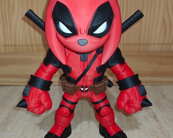 May include: A stylized figurine of a character wearing a red and black suit with a mask featuring white eye patches. The figure has two black swords crossed behind its back, black wrist cuffs with spikes, and a brown utility belt with a circular buckle.