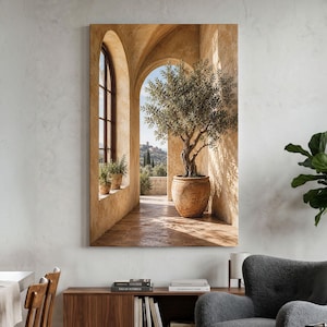 Op de afbeelding: Een verticale wandkunstprint met een zonovergoten stenen boog die een olijfboom in een grote terracotta pot omlijst. De scène toont warme beige muren, een betegelde vloer en een uitzicht op een heuvelachtig landschap in de verte.