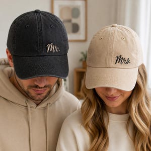 May include: A black baseball cap with the embroidered text Mr. and a beige baseball cap with the embroidered text Mrs. Both caps feature a washed fabric finish, a curved brim, and a structured crown with ventilation eyelets on the top panels.