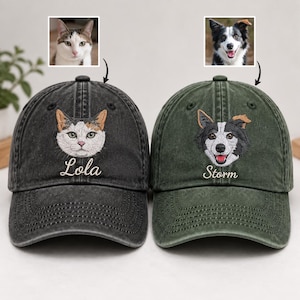 Può includere: Due cappellini da baseball, uno grigio antracite e uno verde oliva, ciascuno con un ricamo personalizzato del muso di un animale. Il cappellino grigio mostra un gatto con il nome Lola, quello verde un cane con il nome Storm, entrambi in bianco.