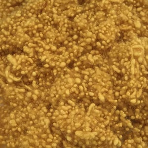May include: Close-up of a pile of mustard-yellow yarn. The yarn has a textured, nubby appearance, with small, irregular bumps and a soft, fuzzy texture. The color is a warm, earthy tone, suggesting a natural fiber.