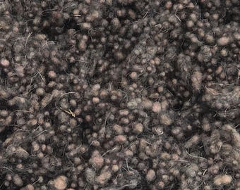 May include: Close-up of a textured fabric with a dense, nubby surface. The material is primarily dark gray with lighter, speckled accents in shades of brown and beige. The fabric appears to be a woven textile, possibly wool or a similar fiber.