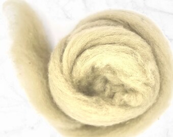 May include: A tightly coiled bundle of light beige wool roving, ideal for fiber art projects. The wool has a soft, fluffy texture and a natural, undyed appearance. The roving is shown against a white marble background.