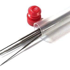 May include: A set of small, metal needle files in a clear plastic tube with a red cap. The files are thin, with pointed ends, and appear to be for detailed work. The tube is partially open, and the files are visible against a white background.