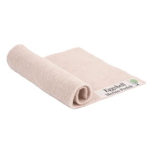 May include: A rolled-up, off-white merino wool prefelt. The fabric is a soft, neutral color, with a slightly textured surface. The label reads "Eggshell Merino Prefelt" with a tree logo.