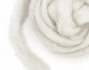 May include: Close-up of a swirl of soft, white wool roving. The wool is tightly wound, creating a textured, circular pattern. The fibers appear fluffy and cloud-like, ideal for crafting projects.