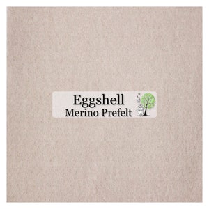 May include: A light beige, textured fabric with a label that reads "Eggshell Merino Prefelt." The label features a tree illustration with a green crown and a gray trunk. The fabric has a soft, felted appearance.