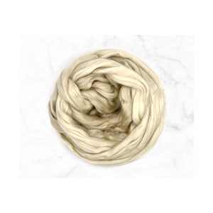 May include: A circular bundle of cream-colored roving yarn, displayed against a white marble background. The yarn appears soft and fluffy, with visible strands and a slightly textured surface. Ideal for fiber art projects.