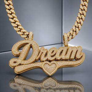 May include: A gold-toned chain necklace featuring a large, script-style pendant that spells out the word Dream. The pendant is encrusted with numerous small, clear stones and includes a heart-shaped detail at the bottom center of the text.