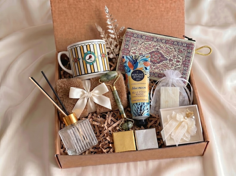 Puede incluir: Una caja de regalo que contiene una taza a rayas con un motivo de p&aacute;jaro, un estuche con cremallera estampado, un tubo de crema de manos y cuerpo Blue Moon, un rodillo facial de jade verde, un difusor de varillas de cristal y un accesorio floral.