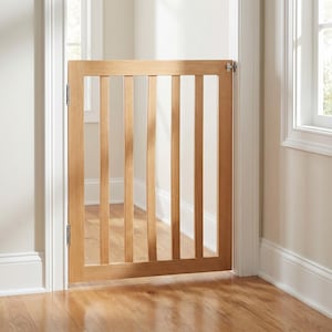May include: A light brown wooden safety gate installed in a doorway. The gate features a rectangular frame with six vertical slats and is attached to the door frame with silver metal hinges on the left side and a latch on the right side.