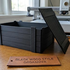 May include: A black rectangular storage box with a slatted design and a matching removable lid. In front of the box lies a rectangular tan leather tag with the text BLACK WOOD STYLE ORGANIZER embossed in black letters on the surface.