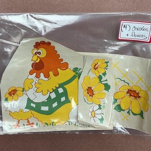 May include: A set of adhesive decals in a clear plastic bag featuring a cartoon chicken wearing a green checkered apron and holding a cracked egg, accompanied by yellow flower designs. A white label with red borders reads (4) Chicken + flowers.