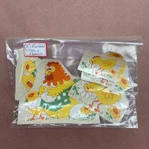 May include: A clear plastic bag containing several adhesive decals featuring yellow chicks, a rooster, and white flowers. A small white label with a red border is attached to the bag, with the handwritten text (5) Rooster Chics + flowers.