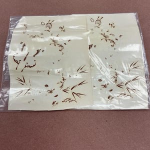 May include: Two rectangular off-white paper sheets enclosed in a clear plastic sleeve. Each sheet features a brown ink illustration depicting bamboo stalks, leaves, and small scattered floral elements arranged in a delicate, sparse pattern.