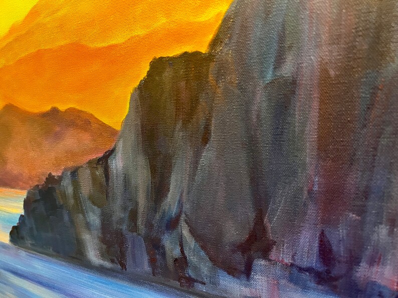 May include: A close-up of a painting depicting a rocky cliff face with a blue and purple water scene in the foreground. The sky is a vibrant orange and yellow.