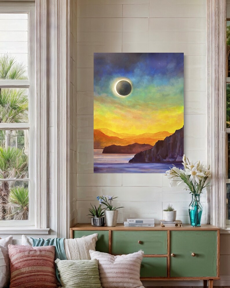 May include: A painting of a solar eclipse over a body of water with mountains in the background. The sky is a vibrant mix of blue, yellow, and green.
