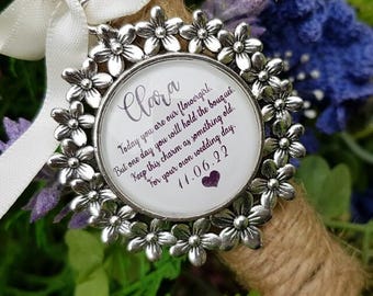 May include: A round silver-toned metal charm featuring a border of small flowers. The centre displays the text: Clara, Today you are our flowergirl. But one day you will hold the bouquet. Keep this charm as something old. For your own wedding day. 11.06.22, with a small purple heart.